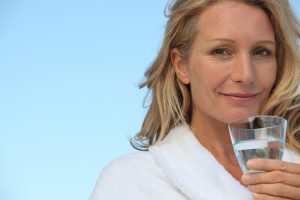 Attractive blonde haired woman with no make up on and drinking a glass of water