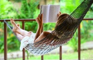 Young woman reading a book lying in a hammock