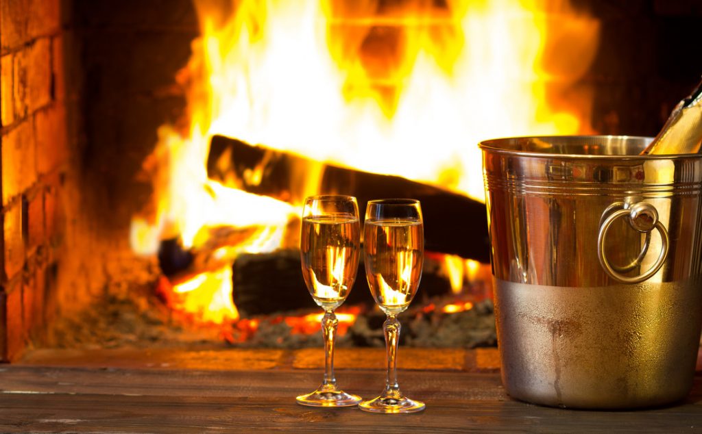 Two glasses of sparkling white wine in front of warm fireplace. Part of a pamper session for an evening of indoor activities.