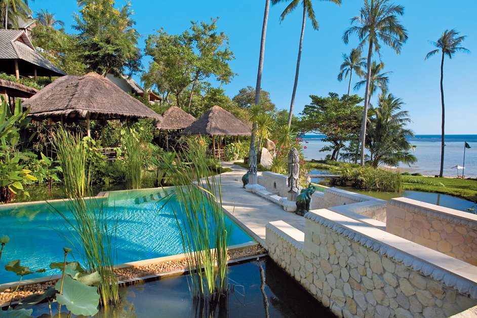 Beautiful outdoor pool next to sea with palm trees and beach huts in Indonesia