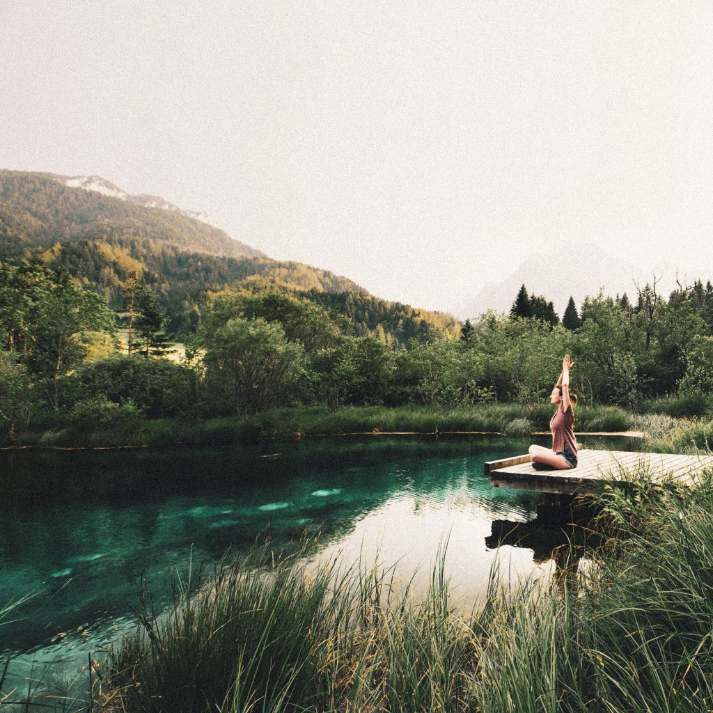 Young woman doing yoga and meditating in lotus position on the background of nature. Concept of Meditation, Relaxation and Healthy Life. Slovenia, Europe. Zelenci Nature reserve