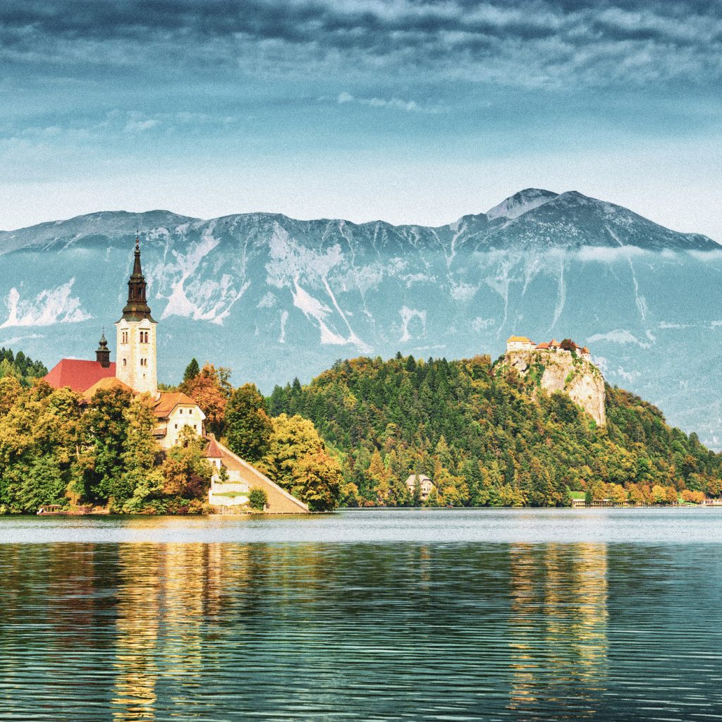 Lake Bled located in Slovenia Europe. There is a Church on the Island and ancient castle on top of a rock. Beautiful blue sky with dramatic cloudscape over the reflection in the Bled Lake. Story in such a beautiful sunny day on sunset. European Alps in the background.