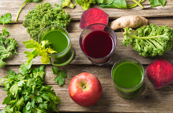 Two glasses of green and one glass of dark red (beetroot) juice on old wooden background, pieces of broccoli, cross section of beetroot , celery sticks, ginger, parsley, apple and curly kale garnishing. High angle view. kapha spadreams