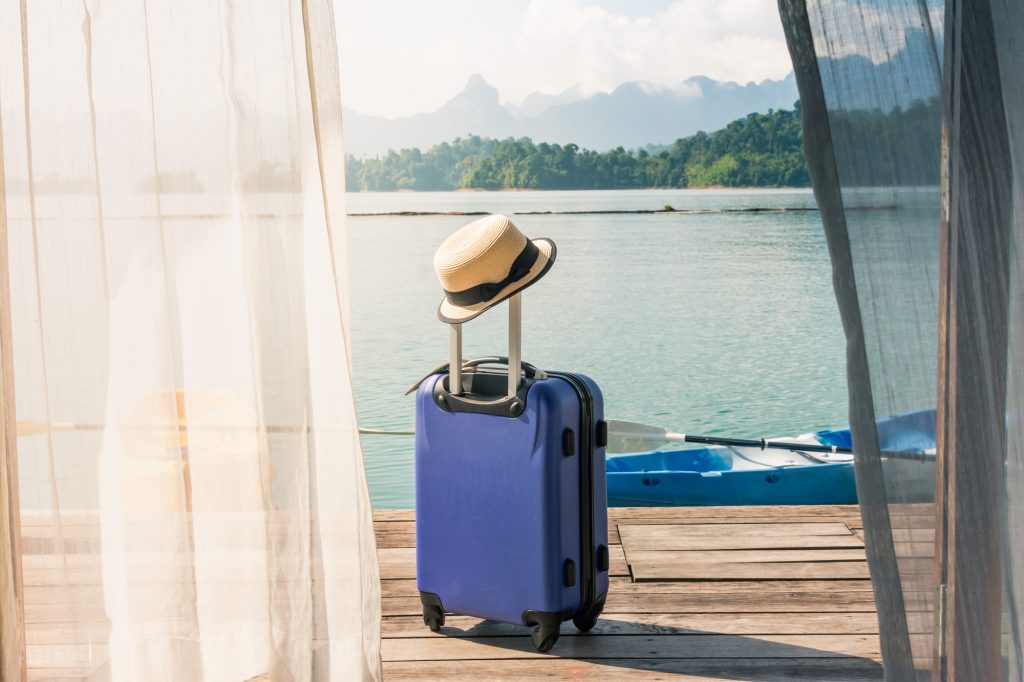 Suitcase on a terrace leading to a lake, a well planned trip with Covid19 travel tips.