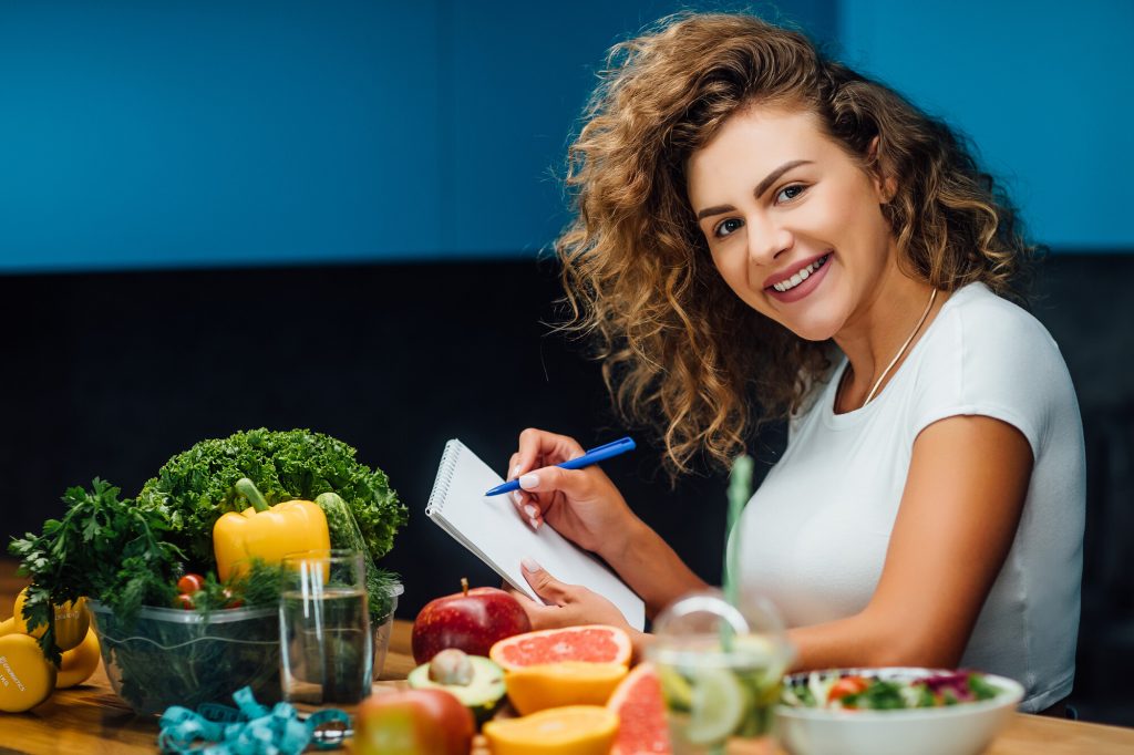 young woman sitting at a table filles with vegetables and fruits planning her pegan diet meals