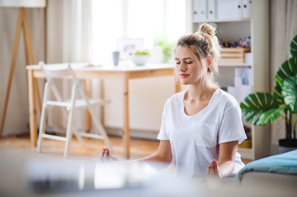 young woman practising yoga in her apartment - Ayurveda and yoga for weight loss